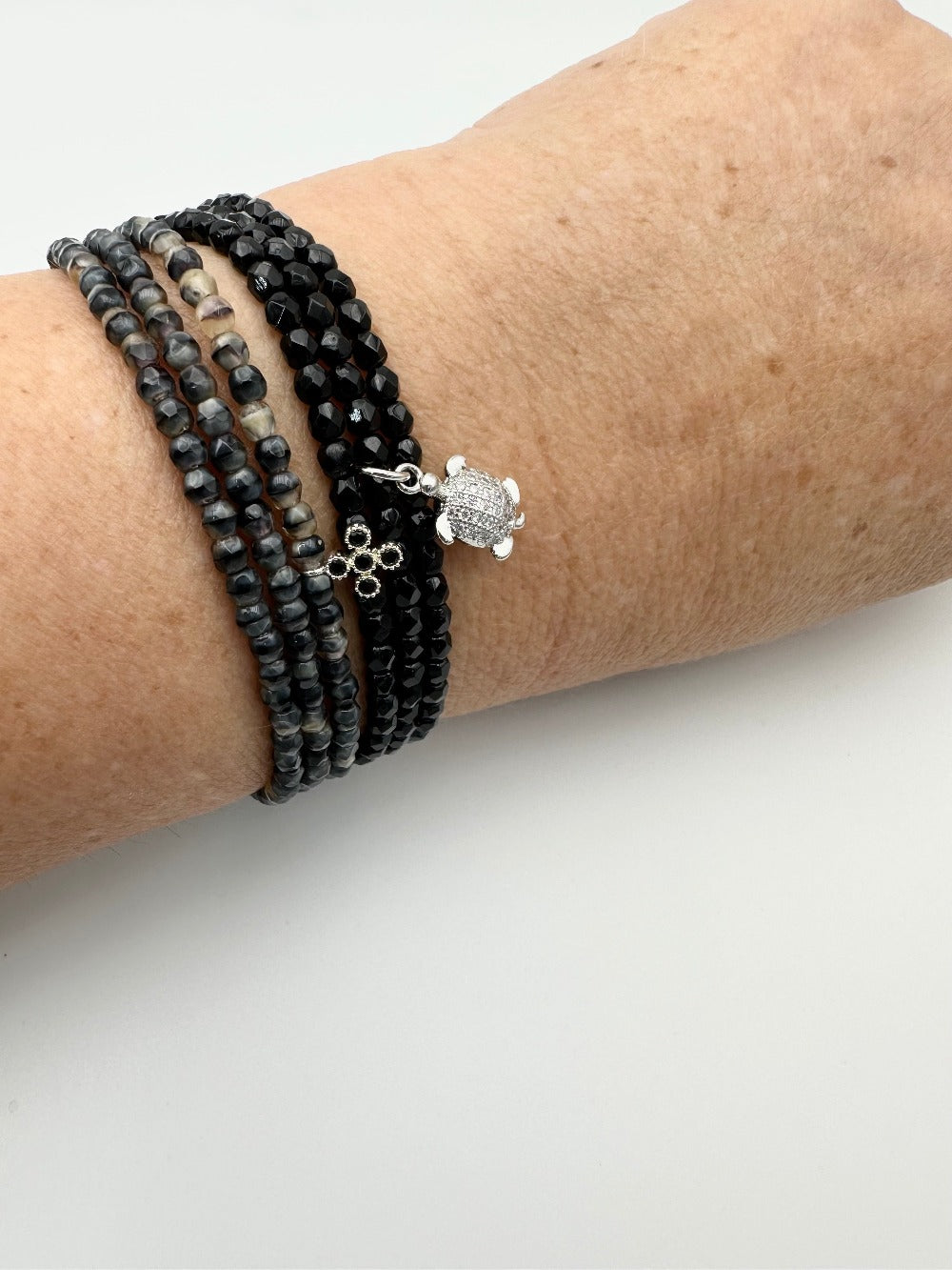 Mix entre deux bracelets en facettes de bohème, un noir avec la petite tortue, un gris et noir marbré avec la petite croix