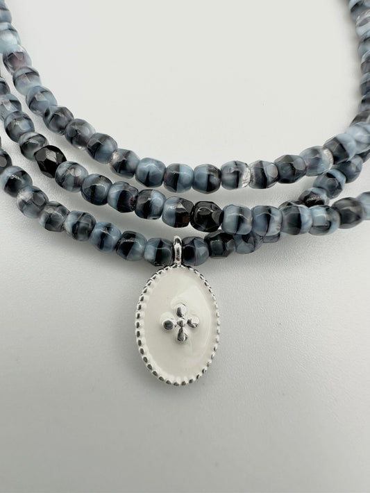 Mon cajoux 2 en 1 en facettes de bohème marbré qui est bleu et noir, avec sa petite breloque ovale, fond blanc, petite croix en argent