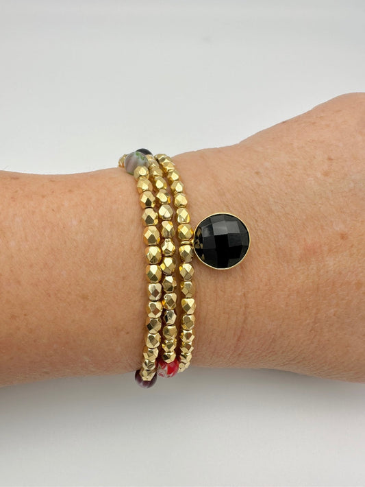 Ce bijou CaJouX est composé de facettes de Bohème couleur Or plaqué 24K sur un fil élastique de grande qualité. On y retrouve aussi des perles rondes Millefiori et ça breloque Onyx noir et plaqué Or.