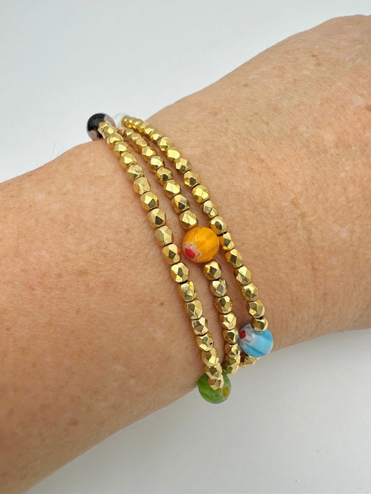 Ce bijou est composé de facettes de Bohème couleur Or plaqué 24K sur un fil élastique de grande qualité. On y retrouve aussi des perles rondes Millefiori.