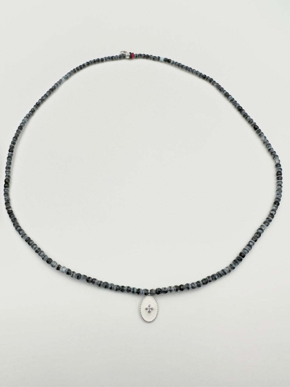 Mon cajoux 2 en 1 en facettes de bohème marbré qui est bleu et noir, avec sa petite breloque ovale, fond blanc, petite croix en argent