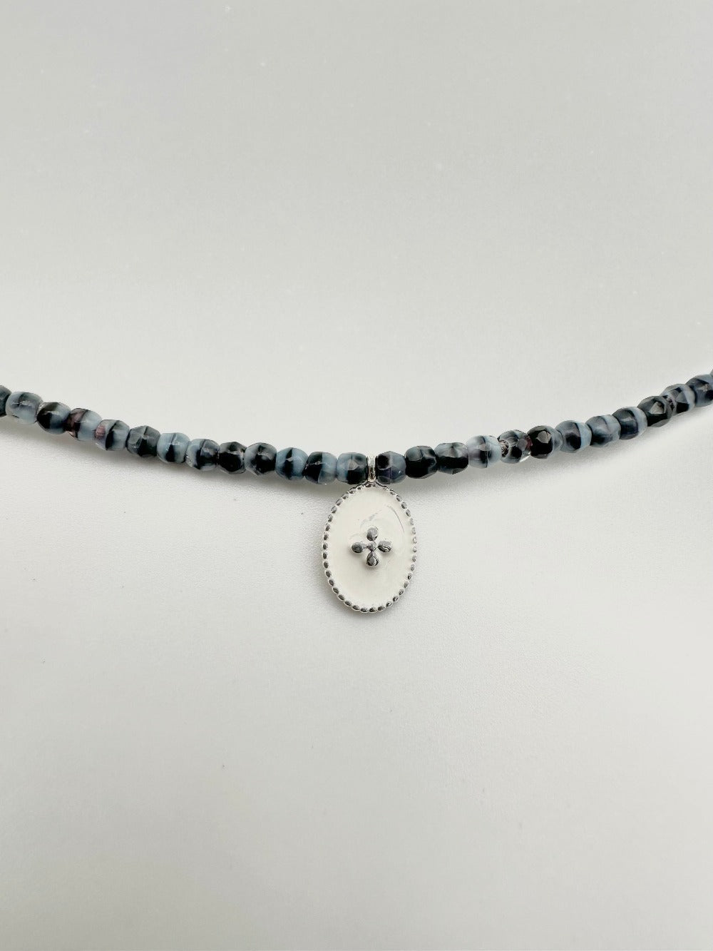 Mon cajoux 2 en 1 en facettes de bohème marbré qui est bleu et noir, avec sa petite breloque ovale, fond blanc, petite croix en argent