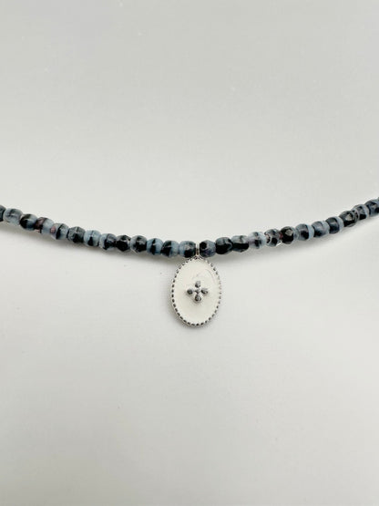 Mon cajoux 2 en 1 en facettes de bohème marbré qui est bleu et noir, avec sa petite breloque ovale, fond blanc, petite croix en argent