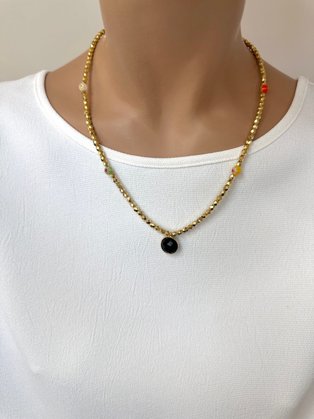 Ce bijou CaJouX est composé de facettes de Bohème couleur Or plaqué 24K sur un fil élastique de grande qualité. On y retrouve aussi des perles rondes Millefiori et ça breloque Onyx noir et plaqué Or.