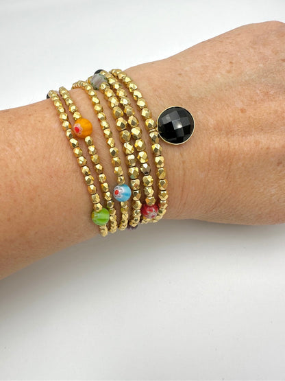 Ce bijou CaJouX est composé de facettes de Bohème couleur Or plaqué 24K sur un fil élastique de grande qualité. On y retrouve aussi des perles rondes Millefiori et ça breloque Onyx noir et plaqué Or.