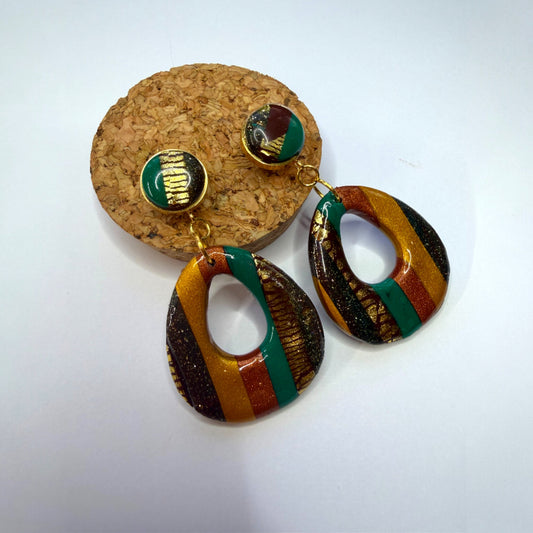 Boucle d'oreille en argile polymère avec du vert, du orange et du doré et du marron sur une base d'acier inoxydable.