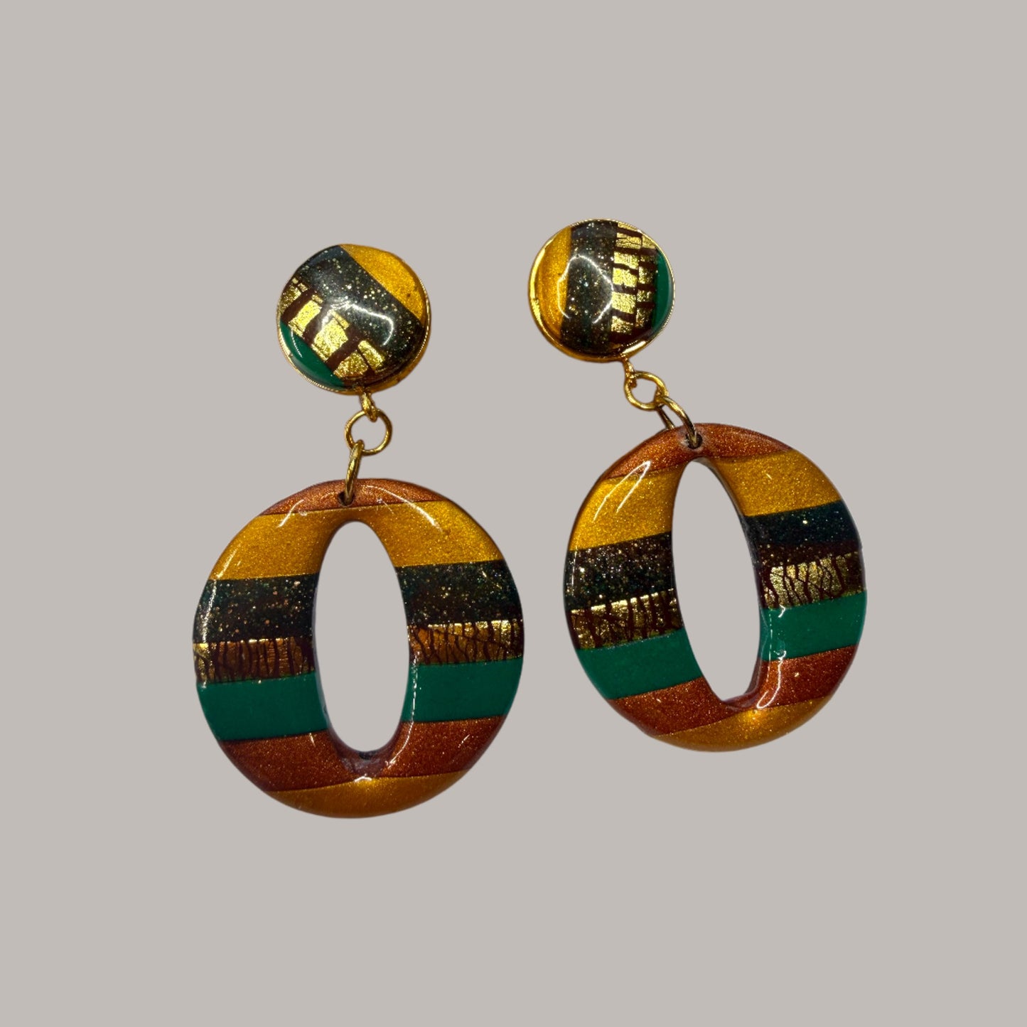 Boucle d'oreille en argile polymère avec du vert, du orange et du doré et du marron sur une base d'acier inoxydable.