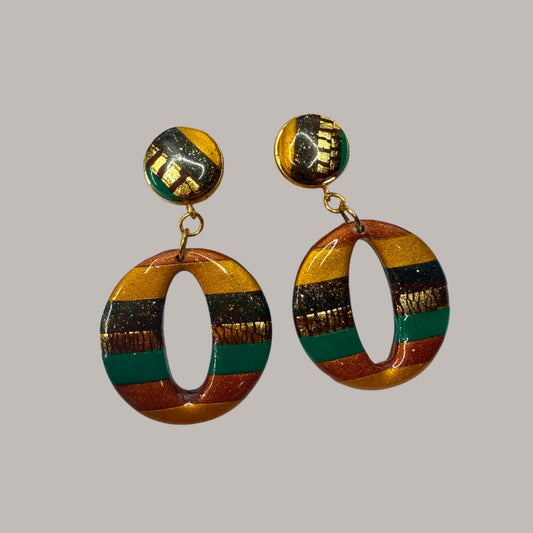 Boucle d'oreille en argile polymère avec du vert, du orange et du doré et du marron sur une base d'acier inoxydable.