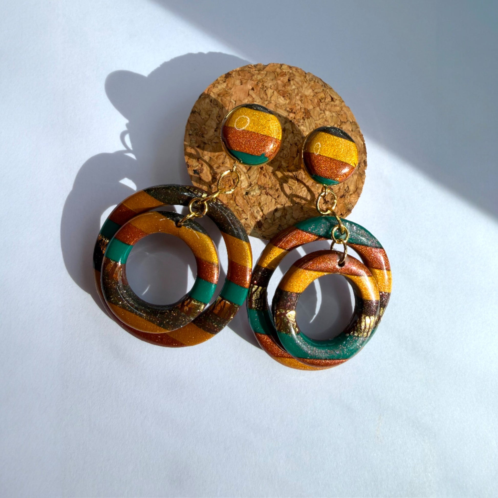 Boucle d'oreille en argile polymère avec du vert, du orange et du doré et du marron sur une base d'acier inoxydable.