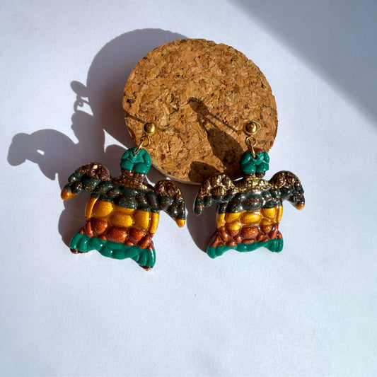 Boucle d'oreille en argile polymère avec du vert, du orange et du doré et du marron sur une base d'acier inoxydable.