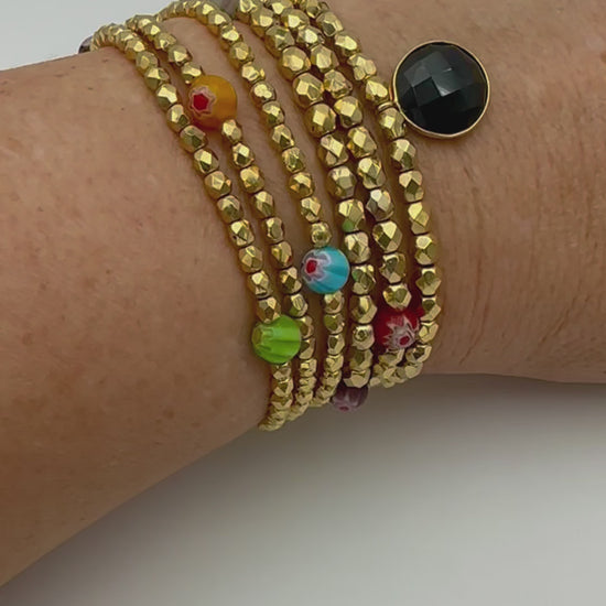 Ce bijou CaJouX est composé de facettes de Bohème couleur Or plaqué 24K sur un fil élastique de grande qualité. On y retrouve aussi des perles rondes Millefiori et ça breloque Onyx noir et plaqué Or.